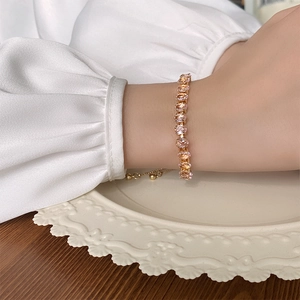 Detail of rose gold bracelet with pink oval zircons on silk background and porcelain plate