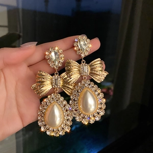 Détail de boucles d'oreilles nœud doré avec perles en goutte et strass scintillants