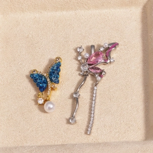 Detailed close-up of butterfly earring with blue enamel and pink gemstone pendant on velvet tray