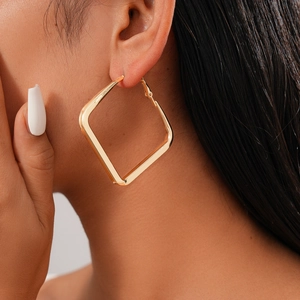 Close-up of a model wearing a minimalist golden square geometric hoop earring