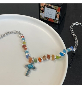Detail of beaded necklace with colorful gravel stones and a blue heart cross pendant