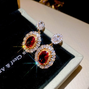 Macro shot of vintage gold-plated oval earrings with red zircon in a luxury jewelry box