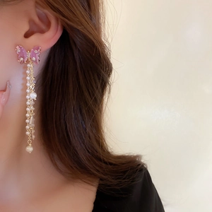 Détail de boucles d'oreilles papillon avec ailes roses, perles et franges dorées