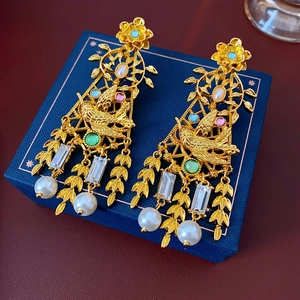Detalle de pendientes vintage dorados con diseño de pájaro, gemas y perlas colgantes