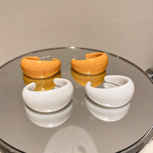 Close-up of orange and white C-shaped resin hoop earrings on a reflective mirror surface