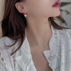 Detailed view of elegant gold heart earrings worn with a white pearl knit cardigan