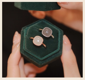 Close-up of vintage square gemstone rings in a green velvet box held by hands