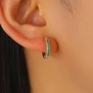 Macro shot of gold-plated hoop earrings with green and white cubic zirconia on ear