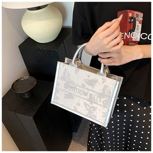 Silver metallic tote bag with butterfly embroidery shown on a model in a cozy home setting