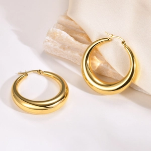 Detail of chunky gold crescent hoop earrings on stone and cream silk background