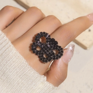 Close-up of a large black crystal interlaced heart ring worn with a knit sweater