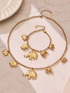 Détail du collier et du bracelet à breloques éléphant en acier doré sur surface en marbre