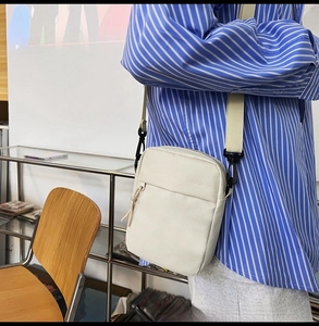 Detail shot of a beige nylon crossbody bag featuring a front zipper pocket and strap