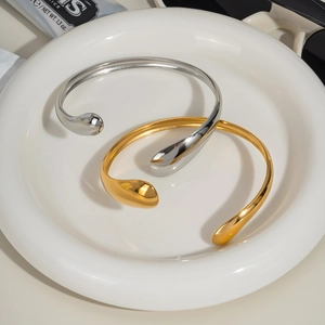 Minimalist wave open bracelets in gold and silver finish on a ceramic plate
