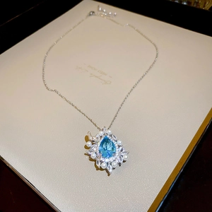 Detail of blue teardrop gemstone pendant with white pearl accents on silver chain
