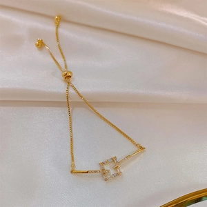 Detail of adjustable gold bracelet with zircon square charm on silk background