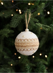 Detail of white velvet Christmas ball with pearl trim and burlap rope hanging on a tree