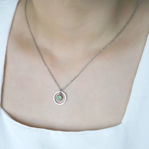Close-up of a silver stainless steel necklace with a round green birthstone on a model