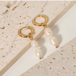 Detail of baroque freshwater pearl earrings with gold hoops on beige marble tiles