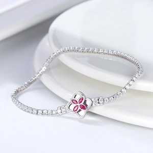 Vista detallada de una pulsera tennis plateada con un dije de trébol de piedras rojas.