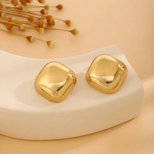 Close-up of golden pillow-shaped earrings on stone pedestal with fountain grass