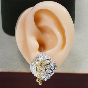 Detail view of silver textured disk earring with golden bow and chain tassels