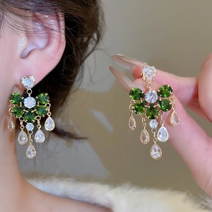 Close-up of gold flower earrings with green drop tassels and sparkling zircon details