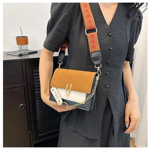 Detail of tricolor crossbody bag featuring suede flap, metal lock, and wide embroidered strap