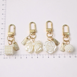 Set of four gold pearl keychains with rose and bow charms shown with a ruler for size
