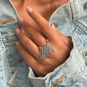 Detail of silver tassel chain ring with beads worn over blue denim background