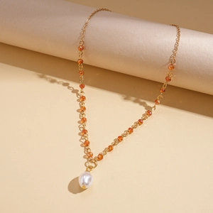 Dettaglio della collana dorata con perle arancioni sfaccettate e grande ciondolo di perla