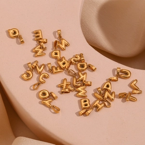 Macro shot of gold-plated 26-letter bubble pendants scattered on pink background
