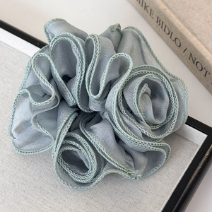 Macro detail of dusty blue satin hair scrunchie with layered floral pleats and texture