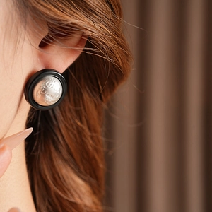 Close-up of vintage round earrings with black matte rim and hammered silver core on model