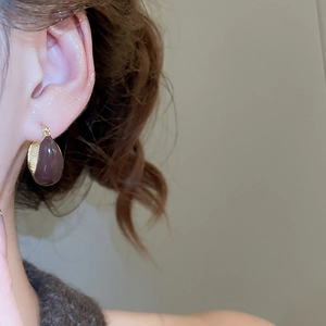 Detail view of a drop-shaped dark brown earring with gold metal clasp on model