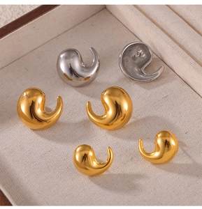 Macro shot of gold and silver comma-shaped twist stud earrings on a beige fabric box