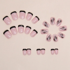 Short French press-on nails with light pink base, black petal designs and silver glitter