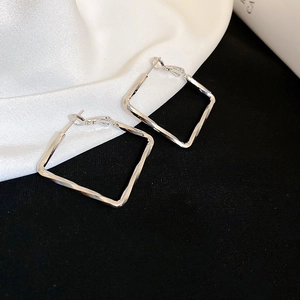 Macro shot of silver geometric square earrings with textured finish on silk backdrop