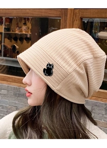 Détail d'une broche chat noir sur un bonnet en maille beige porté par un mannequin