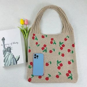 Flat lay of a beige knitted tote bag featuring red cherry patterns with lifestyle props