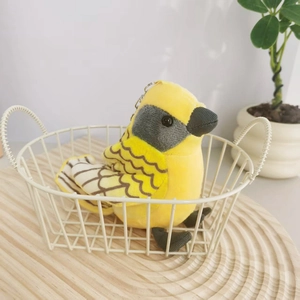 Close-up of a plush yellow bird keychain resting in a white wire basket on a wood tray