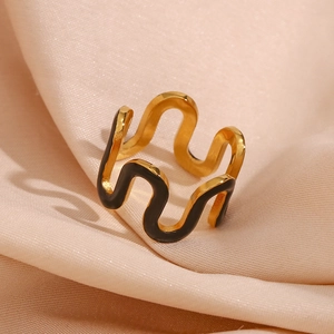 Close-up of gold wave-shaped open ring with black enamel drip detail on silk fabric
