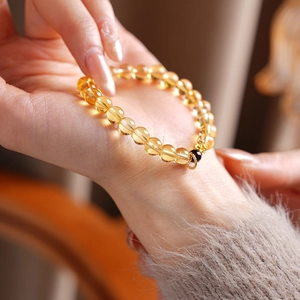 Detail of citrine flower bracelet with garnet bead and golden pendant on woman wrist
