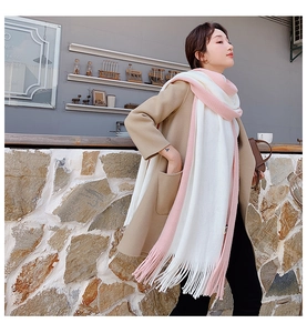 Close-up of a pink and white color-block knit scarf with tassel details on a model