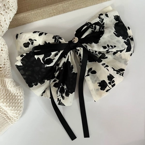 Detail of elegant black and white floral chiffon hair bow with metal button and long ribbons