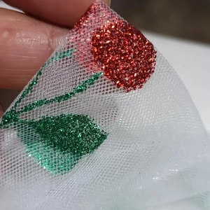 Detailed macro view of white mesh fabric with red and green glitter floral patterns