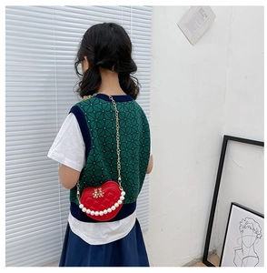 Girl wearing a red heart-shaped quilted mini bag with pearl handle and gold chain strap