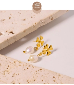 Detail of baroque pearl earrings with golden four-leaf clover stud on marble