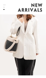 Detail view of black PU leather and beige plush bucket bag worn by model in white blazer