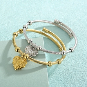Detail of twisted cable bracelets in gold and silver with leaf charms on geometric stands